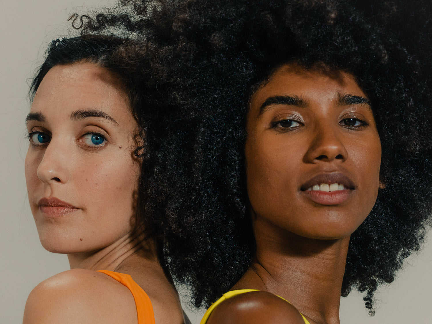 The image features two women standing back-to-back, both looking directly at the camera